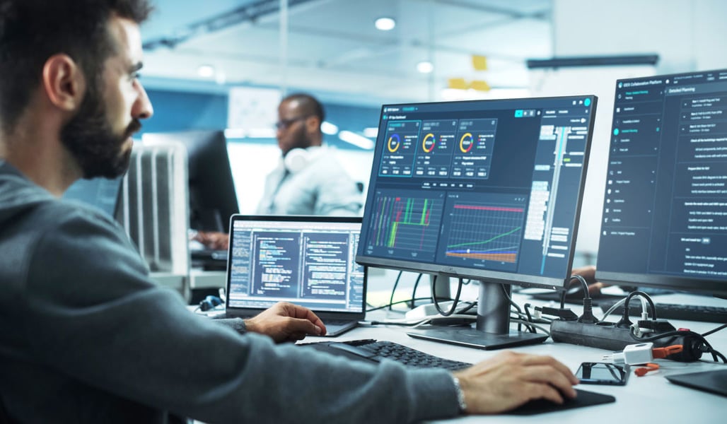 Engineer analyzing well completion data on multiple monitors in a digital operations center, illustrating collaborative software for oil and gas projects.