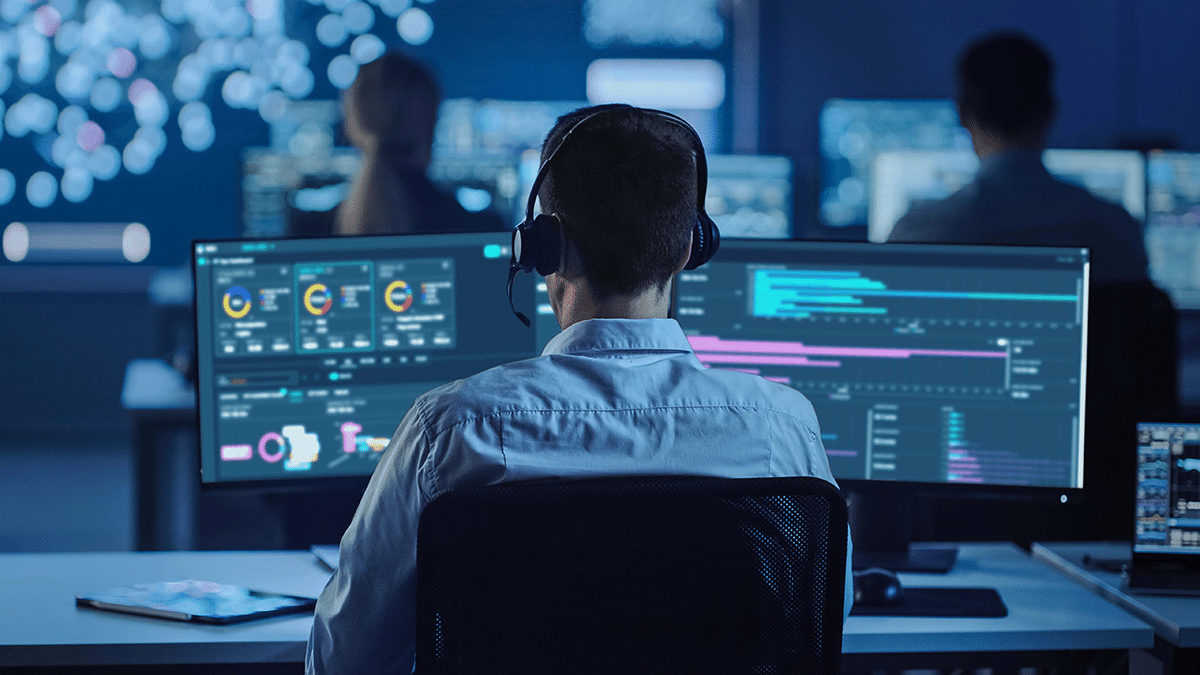 Engineer monitoring digital well intervention data and analytics dashboards on multiple screens in a modern operations center.